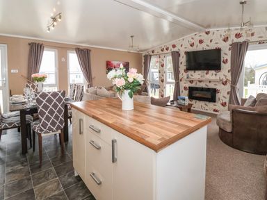 An open living and dining area with a kitchen island a dining table and chairs a sofa and a wall-mounted television at Jonstone Pines in Cayton Bay near Scarborough