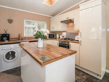 A kitchen with wooden countertops a washing machine a microwave and flowers on the island at Jonstone Pines in Cayton Bay near Scarborough