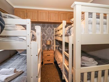 A bedroom with two white bunk beds a bedside table with a lamp and wooden cabinets above at Jonstone Pines in Cayton Bay near Scarborough