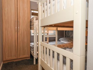 A small bedroom with a wooden wardrobe and two sets of white bunk beds at Jonstone Pines in Cayton Bay near Scarborough