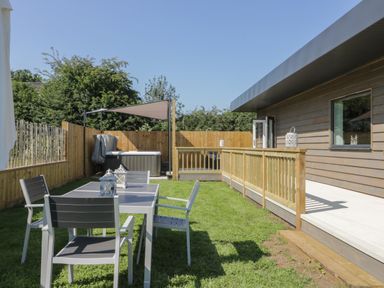 An outdoor area with a table and four chairs on grass a wooden fence a hot tub with a canopy and a wooden deck attached to a building at Bluebell Wood in Brandesburton