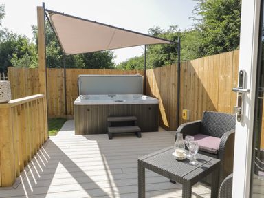 An outdoor patio area with a hot tub under a sunshade and a wicker table and chair set with glasses at Bluebell Wood in Brandesburton