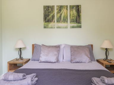 A bedroom with a bed with pillows towels and bedside tables with lamps and a forest triptych on the wall at Bluebell Wood in Brandesburton