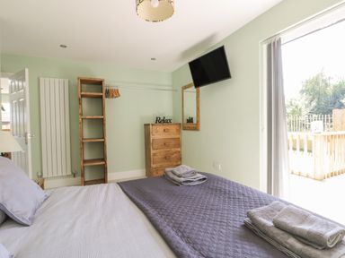 A bedroom with a bed folded towels wooden chest of drawers open closet and wall mounted television at Bluebell Wood in Brandesburton
