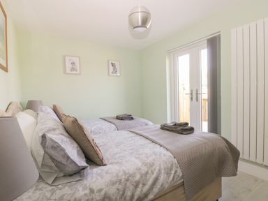 A bedroom with two single beds gray bedding pillows towels on each bed lamp on bedside table framed animal pictures on wall and double doors at Bluebell Wood in Brandesburton