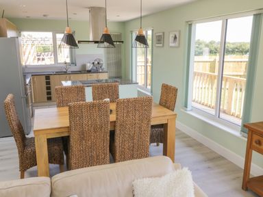 A dining area with a wooden table and six woven chairs next to a kitchen with wooden cabinets and a large window at Bluebell Wood in Brandesburton