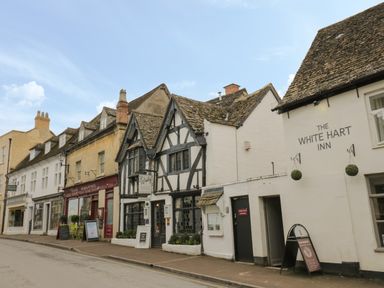 A row of shops and inns with signs and old-style roofs on a street at Thimble Cottage in Winchcombe