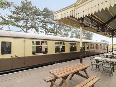 A train station platform with outdoor seating and a train at the platform at Thimble Cottage in Winchcombe