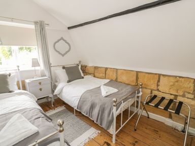 A bedroom with two single beds a small bedside table with a lamp wooden flooring and a small luggage rack at Thimble Cottage in Winchcombe