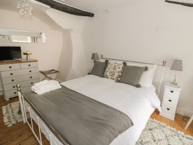 A bedroom with a bed pillows bedside tables lamps a dresser television and wooden floor at Thimble Cottage in Winchcombe