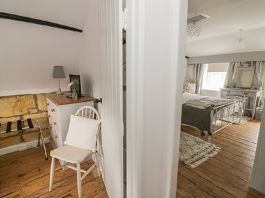 A bedroom with a metal bed frame a dressing table and rugs and a small sitting area with a chair and chest of drawers at Thimble Cottage in Winchcombe