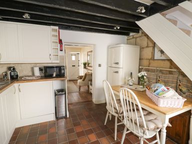 A kitchen with white cabinets a wooden table with chairs and a white refrigerator at Thimble Cottage in Winchcombe