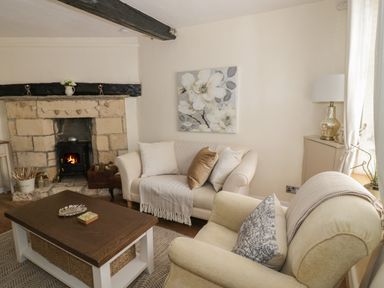 A living room with a stone fireplace two sofas a wooden coffee table and a painting of flowers at Thimble Cottage in Winchcombe