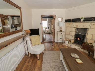 A living room with a fireplace chair coffee table and mirror at Thimble Cottage in Winchcombe