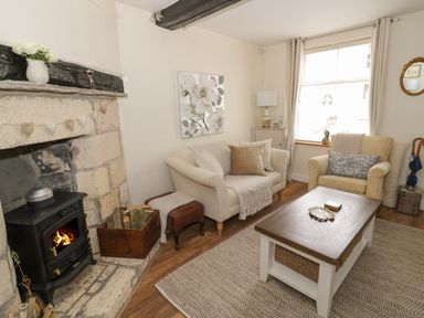 A living room with a fireplace two sofas a wooden coffee table and a window at Thimble Cottage in Winchcombe