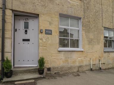 An exterior view of a stone building with a gray door numbered 17 and two potted plants beside the entrance at Thimble Cottage in Winchcombe