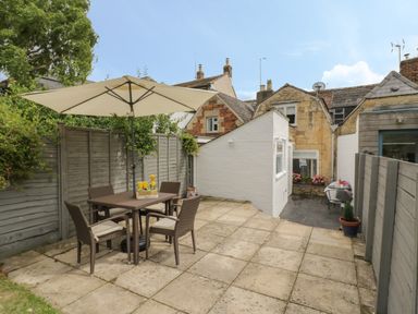 An outdoor patio with a table, four chairs, an umbrella, and potted plants at Thimble Cottage in Winchcombe