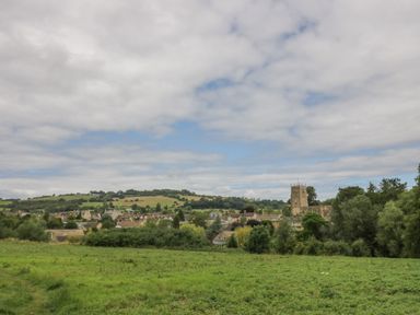 A rural landscape with a village and a church tower surrounded by trees and green fields at Thimble Cottage in Winchcombe
