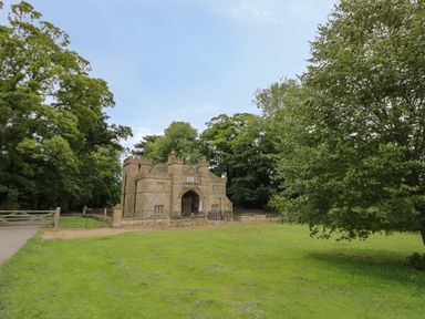 A stone building with an arched entrance surrounded by grass and trees at Thimble Cottage in Winchcombe