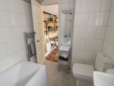 A bathroom with a bathtub toilet towel rack and a mirror showing a view into a dining area at Thimble Cottage Winchcombe