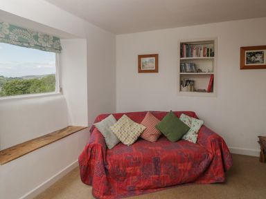 A small sitting area with a red covered sofa and cushions near a window with a wooden sill and built in bookshelf at Athelstan Cottage in Chloe Mead near Stroud