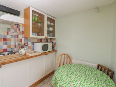 A kitchen corner with a microwave on a wooden countertop and a round table with a green floral tablecloth at Athelstan Cottage Chloe Mead near Stroud