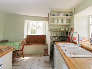 A kitchen with a sink wooden countertops a small table with chairs and shelves with kitchenware at Athelstan Cottage Chloe Mead near Stroud