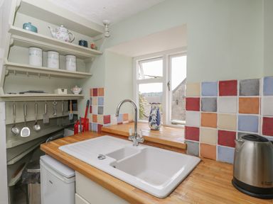 A kitchen sink with wooden countertop colorful tiled backsplash and shelves with kitchen utensils at Athelstan Cottage Chloe Mead near Stroud