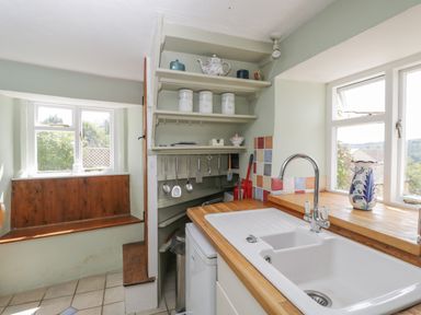 A kitchen with a white sink and faucet wooden countertop shelves with kitchen canisters and utensils near windows at Athelstan Cottage in Chloe Mead near Stroud