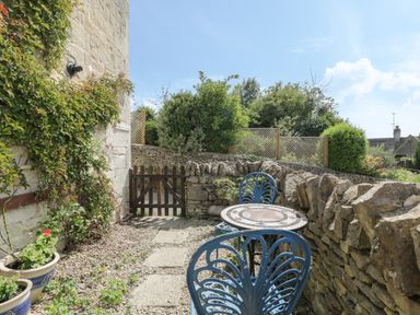 A small outdoor seating area with blue metal chairs and a round mosaic table beside a stone wall at Athelstan Cottage in Chloe Mead near Stroud