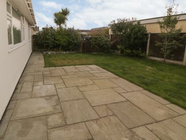 A backyard with a stone tiled patio lawn and shrubs at Glanaig in Morfa Bychan