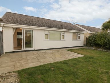 A single story house with sliding glass door a paved patio and a lawn at Glanaig in Morfa Bychan