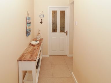A hallway with a wooden topped white console table and a door with frosted glass panels at Glanaig in Morfa Bychan