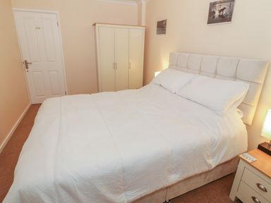 A bedroom with a bed white bedding wardrobe nightstand and lamp at Glanaig in Morfa Bychan