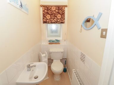 A small bathroom with a toilet a sink a fish shaped mirror and a window with a floral blind at Glanaig Morfa Bychan