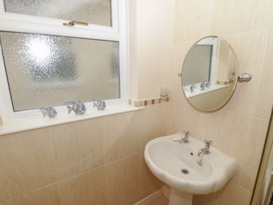 A bathroom sink with a round mirror and three fish decorations on the window sill at Glanaig in Morfa Bychan