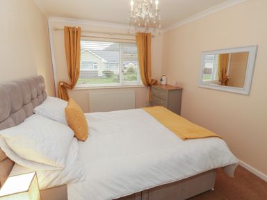 A bedroom with a bed a window with curtains a chest of drawers and a wall mirror at Glanaig Morfa Bychan