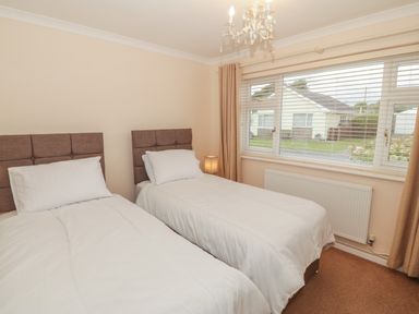A bedroom with two single beds white bedding a window with blinds and beige curtains at Glanaig in Morfa Bychan