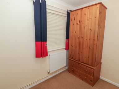 A wooden wardrobe next to a window with blinds and blue and red curtains in a room at Glanaig in Morfa Bychan
