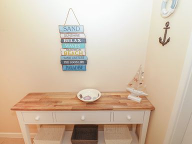 A wooden table with a decorative bowl and a model sailboat under a wall sign with beach words at Glanaig in Morfa Bychan