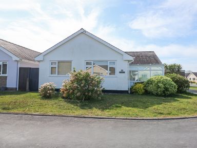A single story white house with shrubs and a lawn at Glanaig in Morfa Bychan
