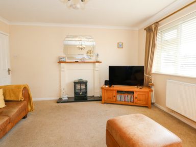 A living room with a television on a wooden stand a fireplace a brown sofa and a window with curtains at Glanaig in Morfa Bychan