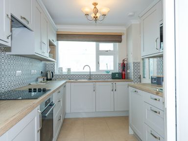 A kitchen with light grey cabinets wooden countertops a patterned tile backsplash a window above the sink and kitchen appliances at Glanaig in Morfa Bychan