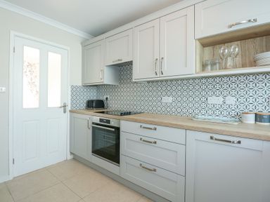 A kitchen with grey cabinets a patterned backsplash an oven a toaster and containers labeled sugar and tea at Glanaig in Morfa Bychan