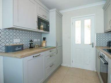 A kitchen with light gray cabinets patterned backsplash microwave oven and various kitchen items on the counter at Glanaig in Morfa Bychan