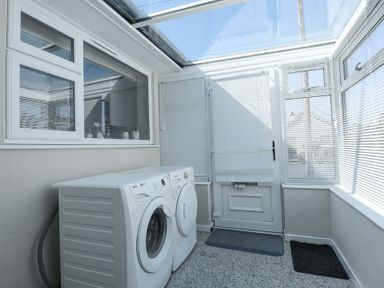 A laundry room with a washing machine and dryer next to a door with window blinds at Glanaig in Morfa Bychan
