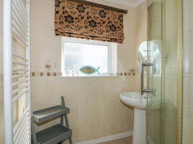 A bathroom with a pedestal sink shower cubicle towel rail window with blind and a two tier shelf at Glanaig in Morfa Bychan