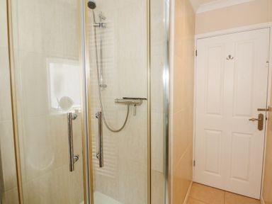 A shower with glass doors and a white door in a bathroom at Glanaig in Morfa Bychan