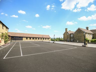 An outdoor tennis court with surrounding buildings and lampposts at Norton Cottage in Craven Arms