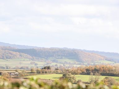A rural landscape with fields trees and hills under a cloudy sky at Norton Cottage in Craven Arms